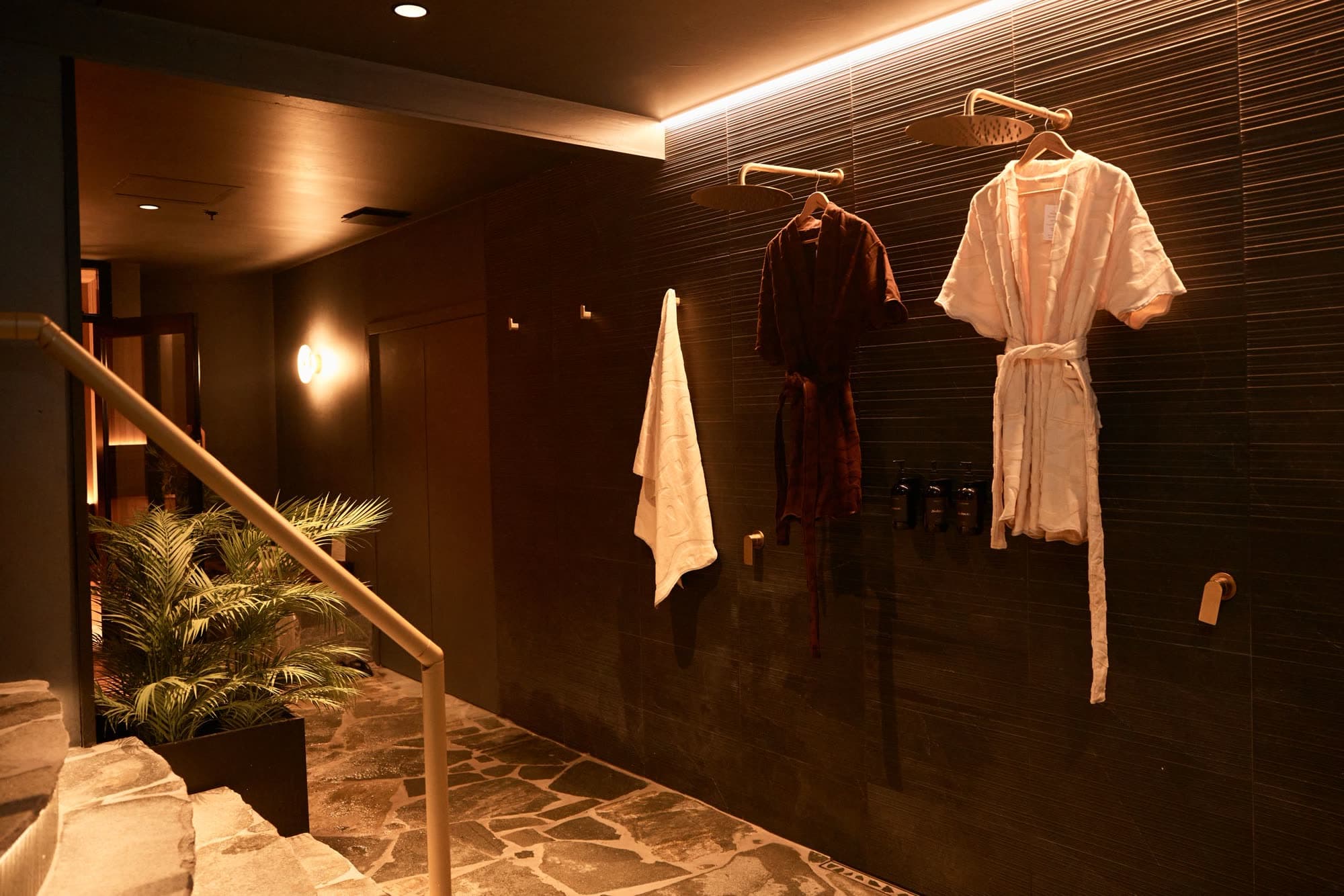 A dark tiled changing room with SENA robes hanging on a brass rail