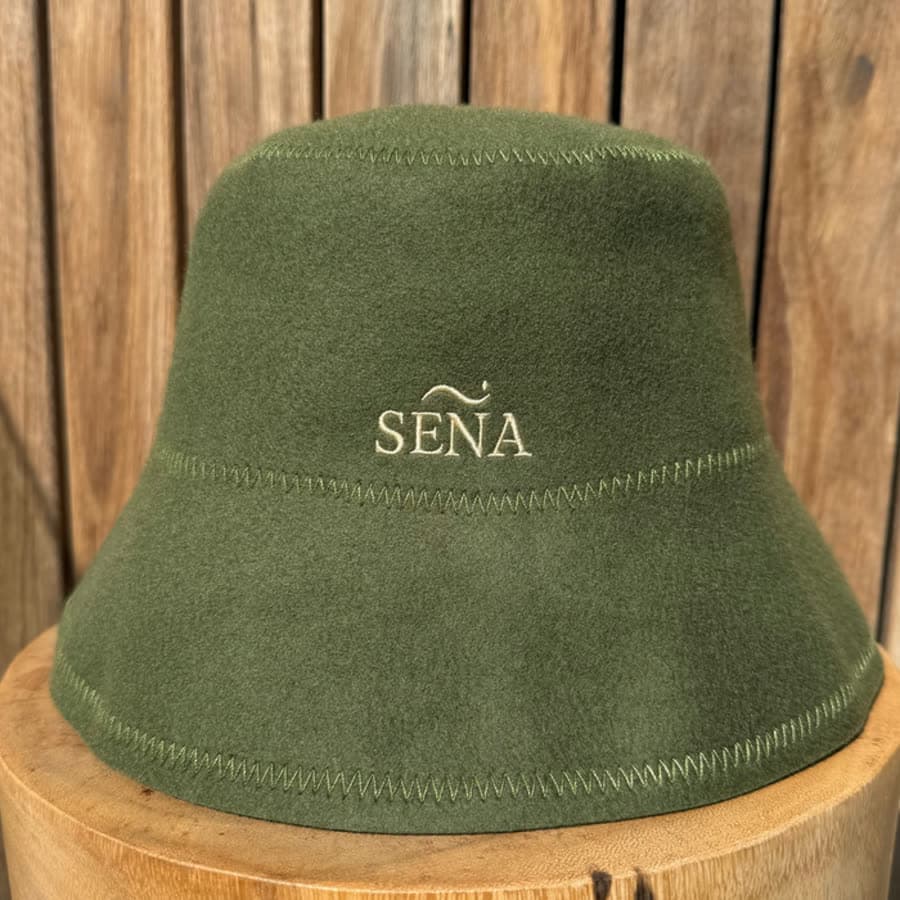 An olive SENA merino sauna hat on a timber block