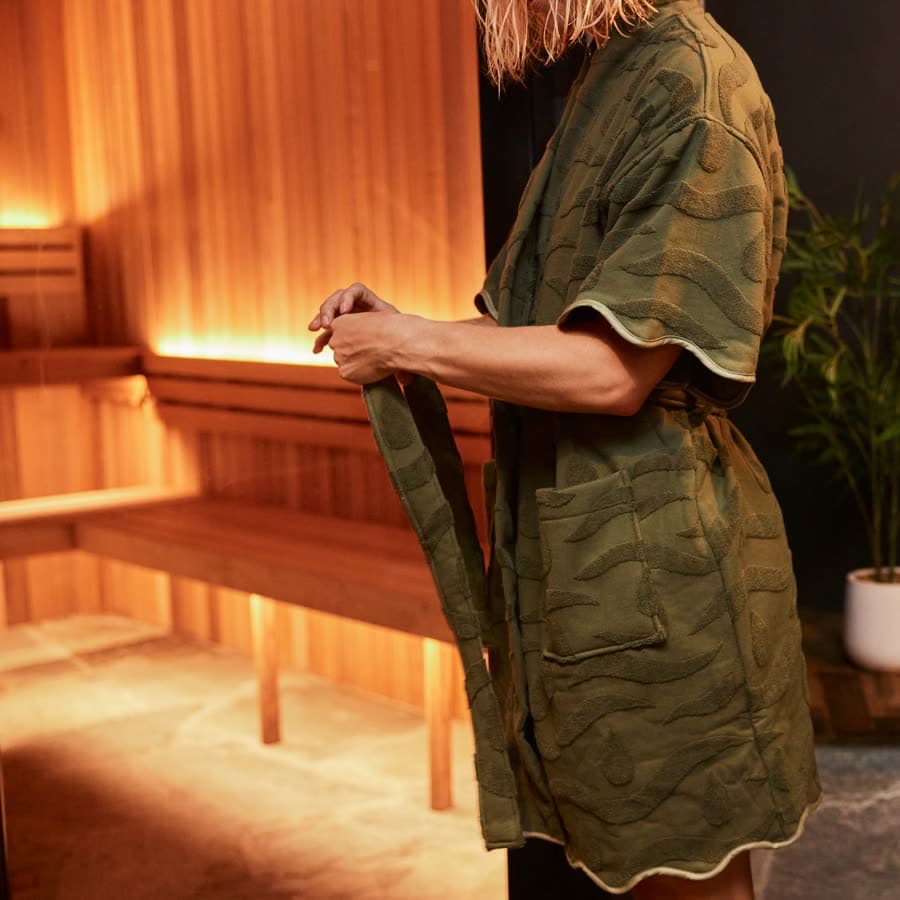An olive SENA jacquard robe being tied, in a cedar sauna